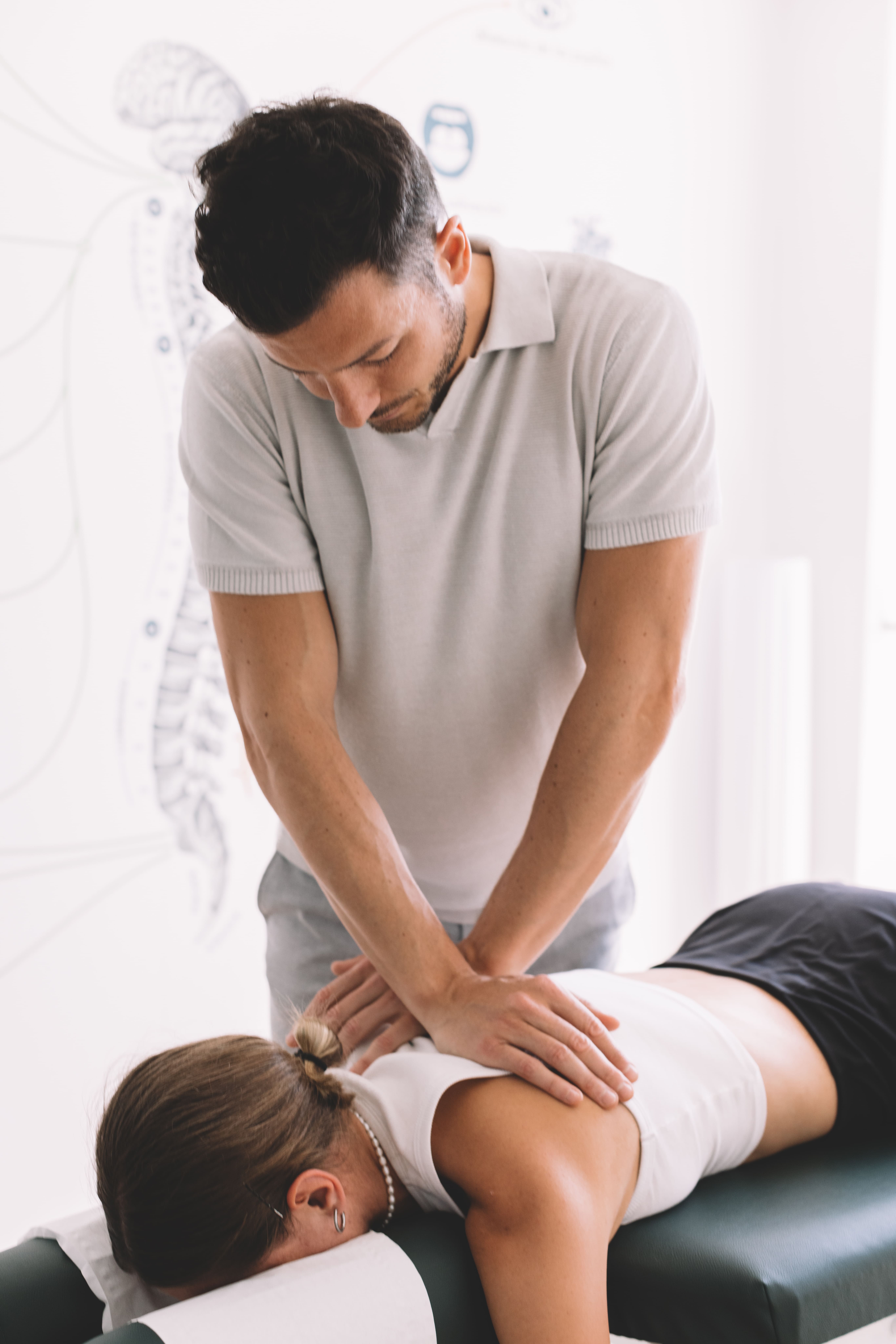 Estres-quimico-y-alimentacion-quiropractica: Mujer estirada boca abajo en una camilla de quiropráctica y hombre quiropráctico poniendo sus manos sobre la espalda de la mujer.